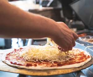 Pizza maker topping a pizza with fresh mozzarella